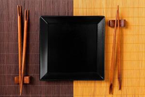 Empty black square slate plate with chopsticks for sushi on wooden background. Top view with copy space photo