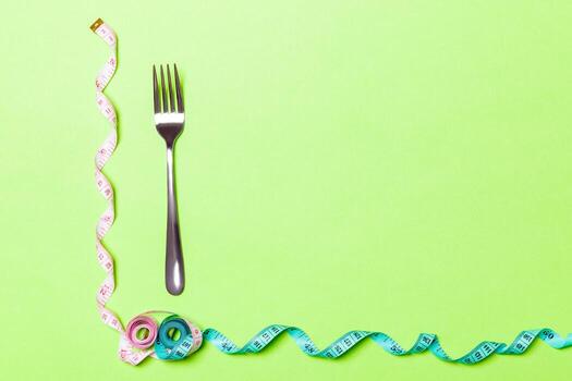 Diet concept with fork and measuring tape on green background. Top view of weight loss with empty space photo