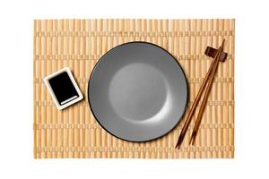 Empty round gray plate with chopsticks for sushi and soy sauce on yellow bamboo mat background. Top view with copy space for you design photo