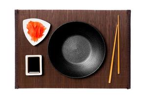Empty round black plate with chopsticks for sushi, ginger and soy sauce on dark bamboo mat background. Top view with copy space for you design photo