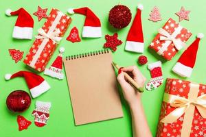 Top view of female hand making some notes in noteebok on green background. New Year decorations and toys. Christmas time concept photo