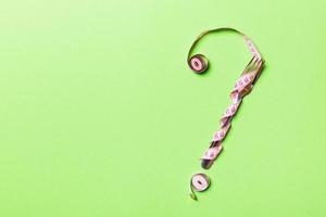 Top view of question mark made of fork and measuring tape on green background. Diet concept with copy space photo