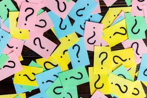 Too Many Questions on wooden background. Pile of colorful paper notes with question marks. top view photo