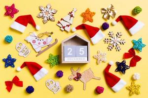 Top view of wooden calendar with Christmas decorations and Santa hats on yellow background. The twenty fifth of December. Happy holiday concept photo