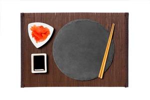 Emptyround black slate plate with chopsticks for sushi, ginger and soy sauce on dark bamboo mat background. Top view with copy space for you design photo