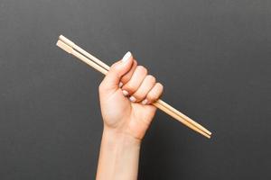 Woman's hand holding chopsticks on black background. Chinese food concept with empty space for your design photo