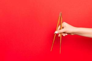 Wooden chopsticks holded with female hands on red background. Ready for eating concepts with empty space photo