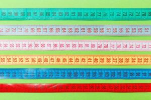 Close up of a group of colorful measure tapes lying in rows as a background. Diet concept on green background photo