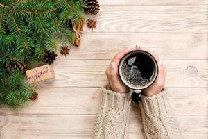 female hands holding coffee cupon wooden table with chrisstmas decoration. Top view with copy space photo