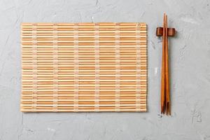 two sushi chopsticks with empty bamboo mat or wood plate on stone Background Top view with copy stace photo