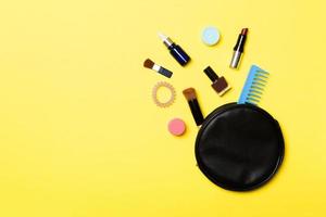 Top view of make up products fallen out of cosmetics bag on yellow background. Cosmetic concept with space for your design photo