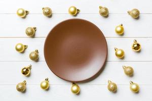 Top view of festive plate with golden baubles on wooden background. Christmas decorations and toys. New Year advent concept photo