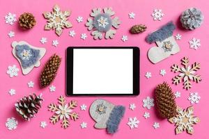 Top view of digital tablet, holiday toys and decorations on pink Christmas background. New Year time concept photo