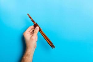 Crop image of male hand holding chopsticks on blue background. Japanese food concept with copy space photo