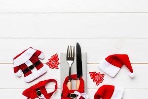 Festive set of fork and knife on wooden background. Top view of new year decorations and santa clothes and hat. Christmas concept with copy space photo