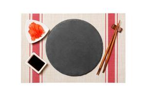 Emptyround black slate plate with chopsticks for sushi and soy sauce, ginger on sushi mat background. Top view with copy space for you design photo