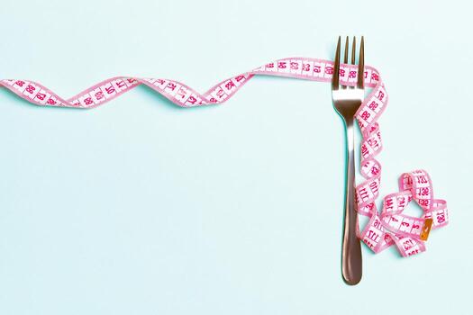 Fork and curled measuring tape are on blue background with top view. Concept of diet for weight loss and space for your design photo
