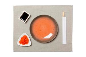 Empty round brown plate with chopsticks for sushi, ginger and soy sauce on grey napkin background. Top view with copy space for you design photo