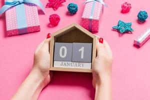 vista superior de las manos femeninas sosteniendo el calendario sobre fondo rosa. el primero de enero. decoraciones navideñas. concepto de año nuevo foto