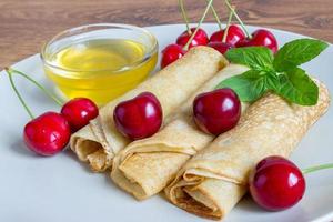 Homemade dessert. Fried pancakes with honey. Crepe with cherry on white plate background. photo