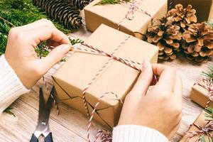 Woman wrapping christmas present , girl prepares xmas gifts with fir tree and pine cone. Hand crafted gift on wooden background with Christmas decor. Top view, copy space. Toned photo