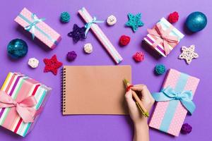 Top view of female hand making some notes in noteebok on colorful background. New Year decorations and toys. Christmas time concept photo