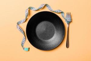 Strict diet concept with empty space fro your design. Top view of plate with fork in measuring tape on orange background photo