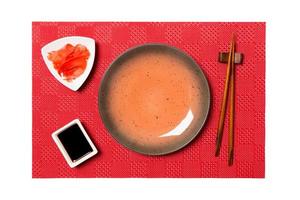 Empty round brown plate with chopsticks for sushi and soy sauce, ginger on red mat sushi background. Top view with copy space for you design photo