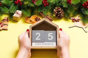 Top view of female hands holding calendar on yellow background. The twenty fifth of December. Holiday decorations. Christmas time concept photo