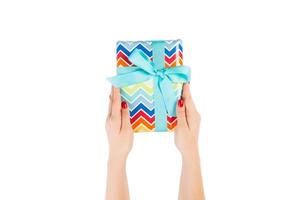 Woman hands give wrapped Christmas or other holiday handmade present in colored paper with blue ribbon. Isolated on white background, top view. thanksgiving Gift box concept photo