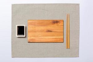 Empty rectangular brown wooden plate with chopsticks for sushi and soy sauce on grey napkin background. Top view with copy space for you design photo