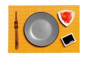 Empty round gray plate with chopsticks for sushi and soy sauce, ginger on yellow bamboo mat background. Top view with copy space for you design photo