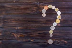 signo de interrogación de monedas de diferentes países sobre un fondo de madera foto
