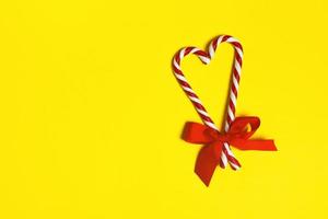 Two Christmas candy canes overlapping to form a heart and a red bow on a yellow background. copy space photo