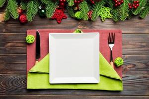 Top view of New Year dinner on festive wooden background. Composition of plate, fork, knife, fir tree and decorations. Merry Christmas concept photo