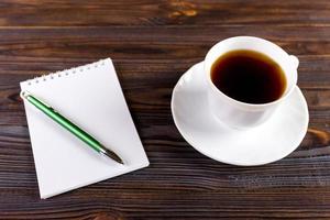 White cup of hot coffee and white sketch book on wood table photo