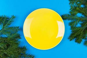 yellow empty ceramic plate on a blue background is decorated with a Christmas branch. view from above photo