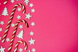 Christmas candy cane lied evenly in row on pink background with decorative snowflake and star. Flat lay and top view photo