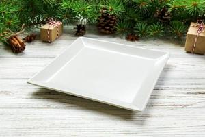vista de perspectiva. plato cuadrado blanco vacío sobre fondo de Navidad de madera. concepto de plato de cena navideña con decoración de año nuevo foto