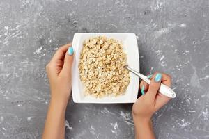 Useful and healthy breakfast. The girl took milk to pour it into oatmeal on a gray background, top view photo