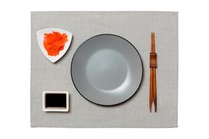 Empty round gray plate with chopsticks for sushi, ginger and soy sauce on grey napkin background. Top view with copy space for you design photo