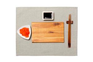 Empty rectangular brown wooden plate with chopsticks for sushi, ginger and soy sauce on grey napkin background. Top view with copy space for you design photo