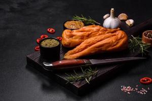 Tasty smoked fillet of chicken breast with spices and herbs on a wooden cutting board photo