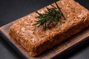 Tasty meat brawn or roll on a wooden cutting board with spices and herbs photo