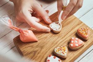 Woman hand decorate cookies in shape of heart, closeup photo