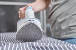 Steam boost on the modern iron. Woman ironing clothes with modern iron photo