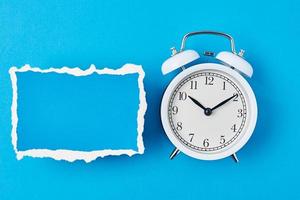 White alarm clock and empty torn paper sheet on a blue background photo