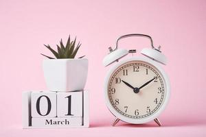 Alarm clock and wooden calendar blocks with date 1 march on the pink background.