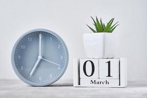 Alarm clock with wooden block calendar date 1st march and plant on the table photo