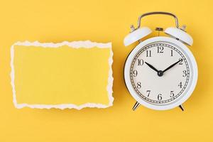 White alarm clock and empty torn paper sheet on a yellow background photo